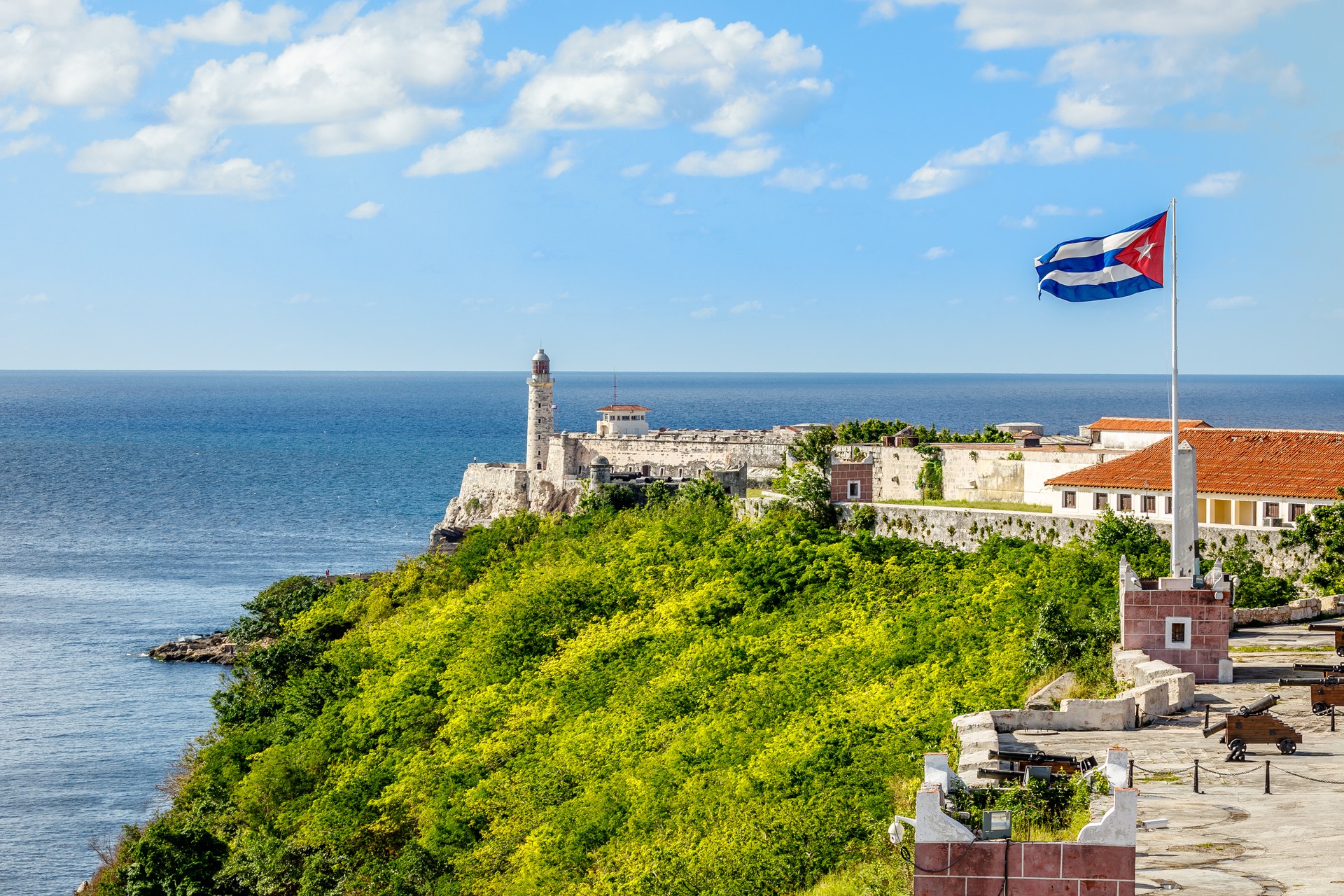 El Morro Spanish fortress with lighthouse, cannons and Cuban flag in th foreground, with sea in the background, Havana, Cuba