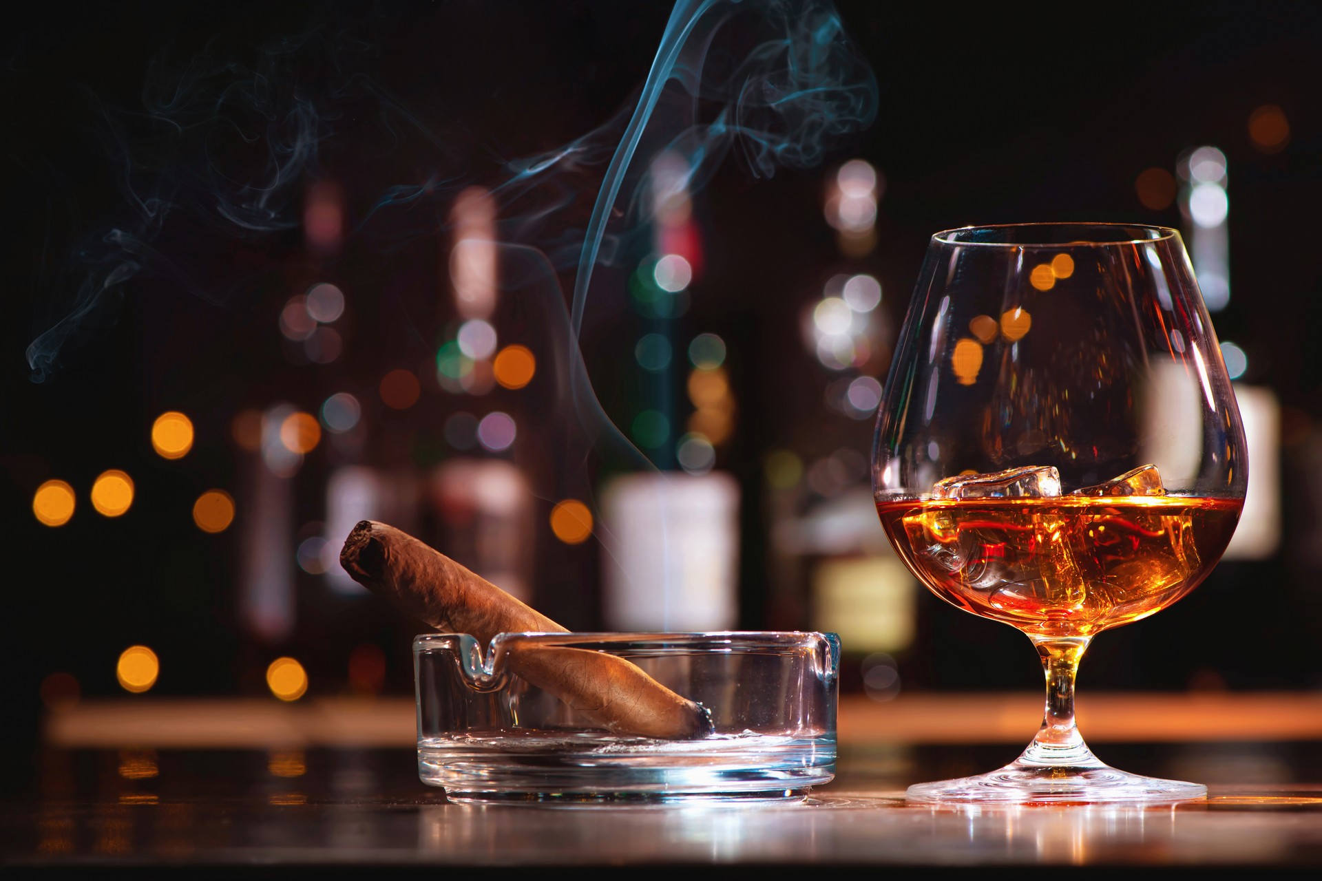 Glass of whiskey or cognac with ice cubes and smoking cigar